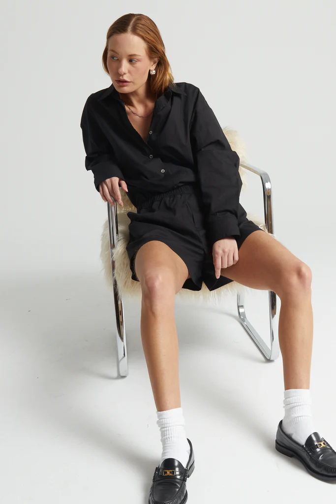 Woman sitting on a chair wearing a black outfit with white socks and black shoes.