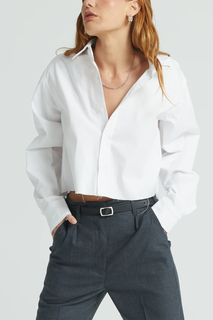 Person wearing a white shirt and dark pants on a plain background