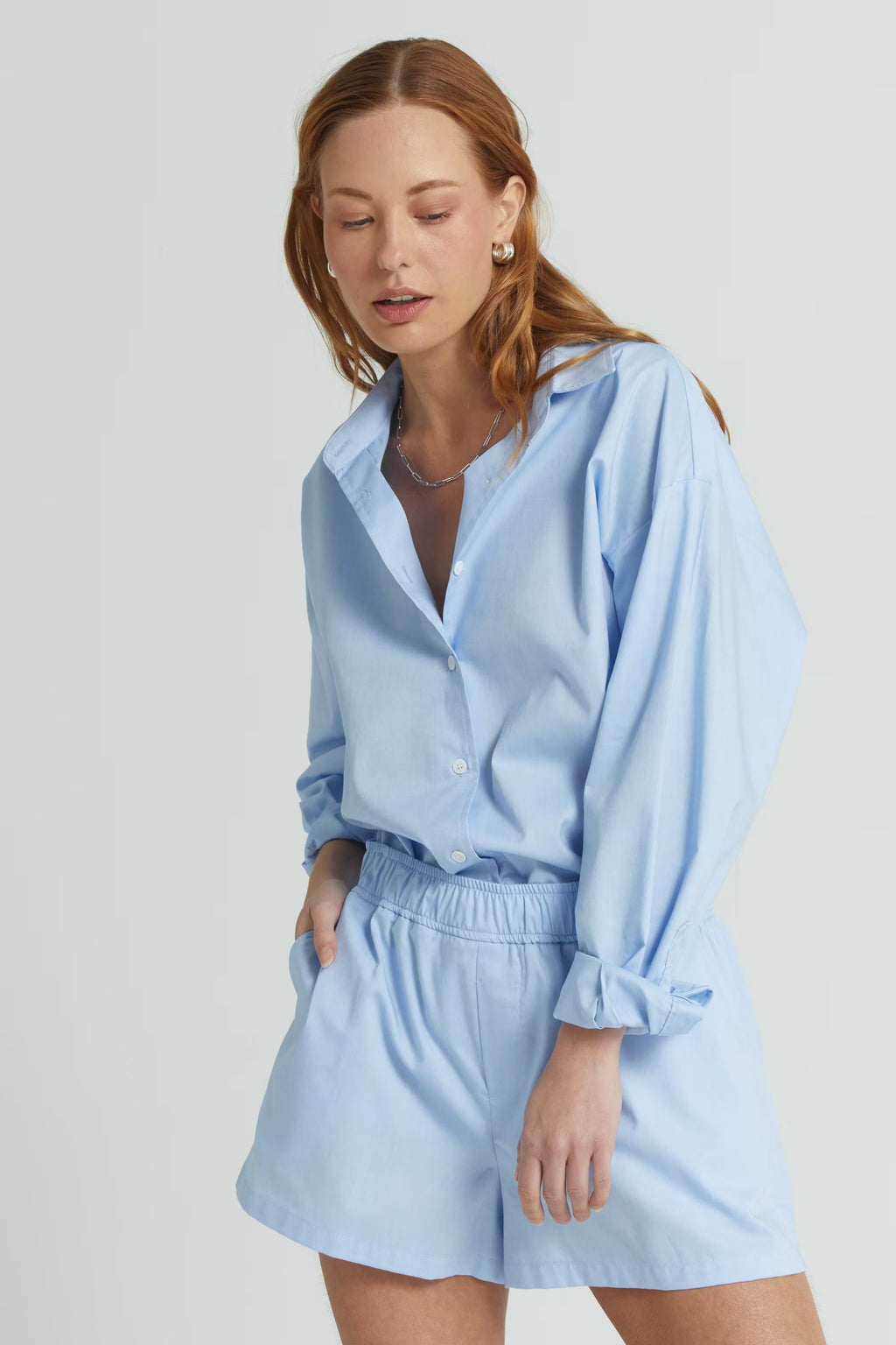 Woman wearing a light blue shirt and shorts set on a plain background