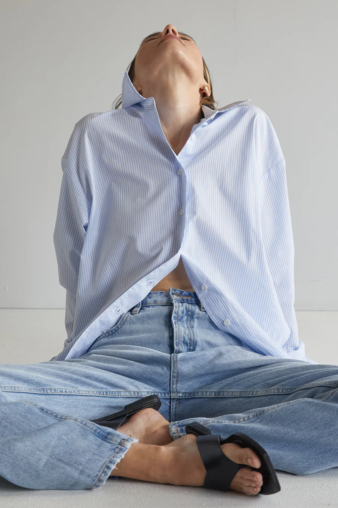 Person wearing a light blue oversized shirt and jeans sitting on the floor.