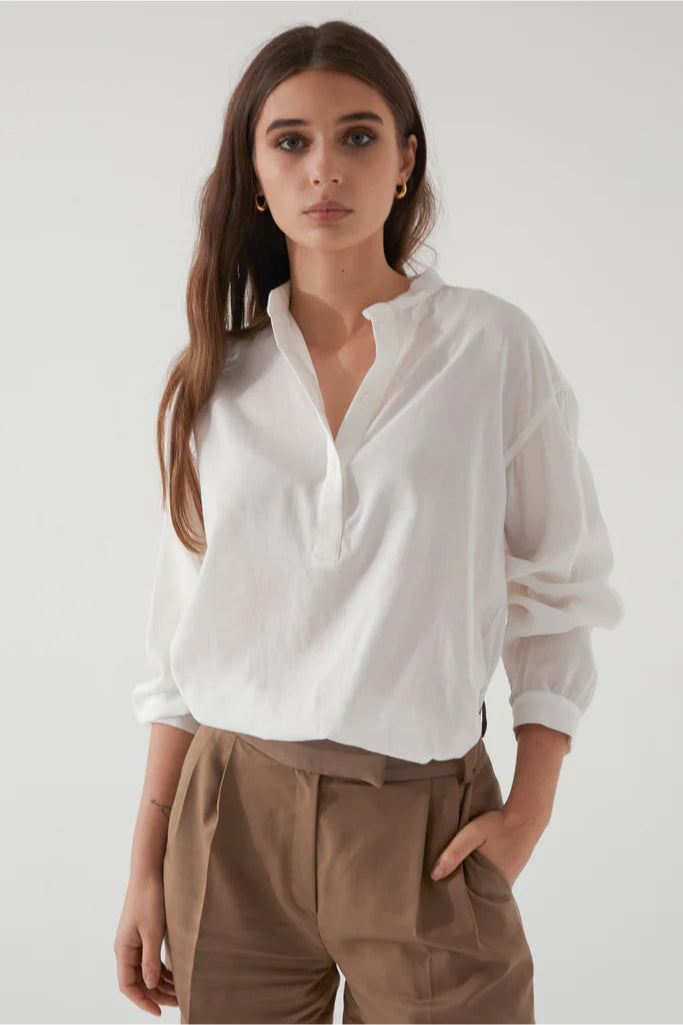 Woman wearing a white shirt and brown pants against a plain background