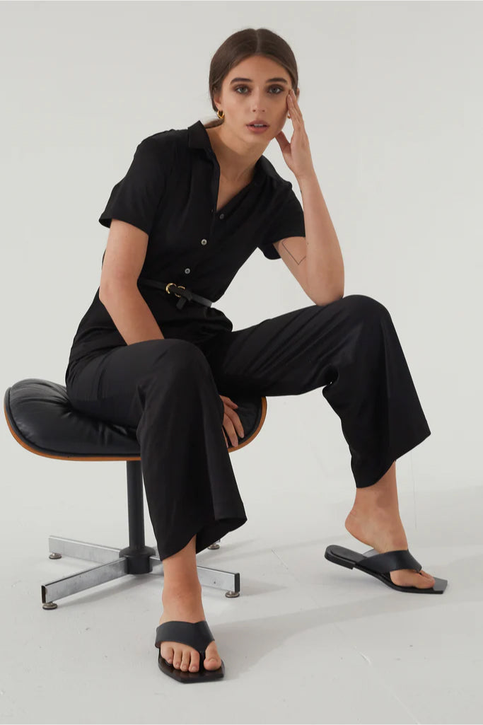 Woman in a black jumpsuit sitting on a chair against a white background