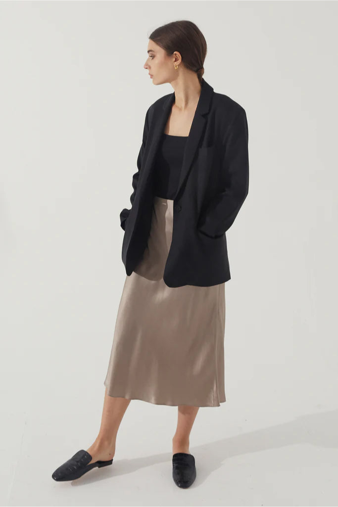 Woman wearing a black blazer, black top, and beige skirt on a white background