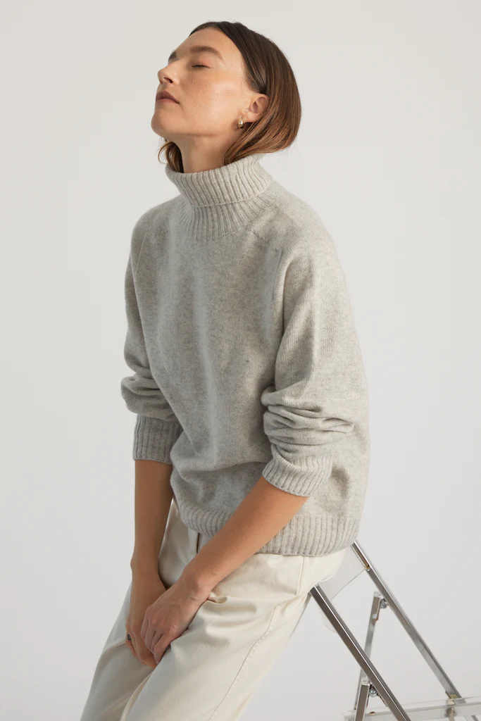 Person wearing a light gray turtleneck sweater against a white background