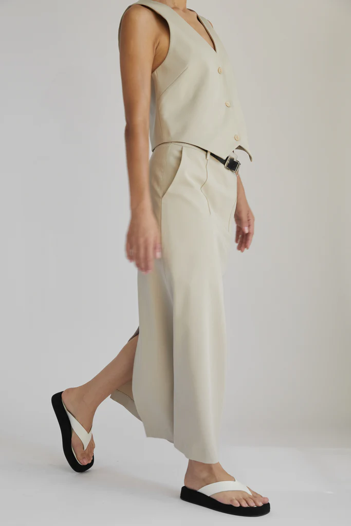 Woman wearing a beige sleeveless top and wide-leg pants on a white background