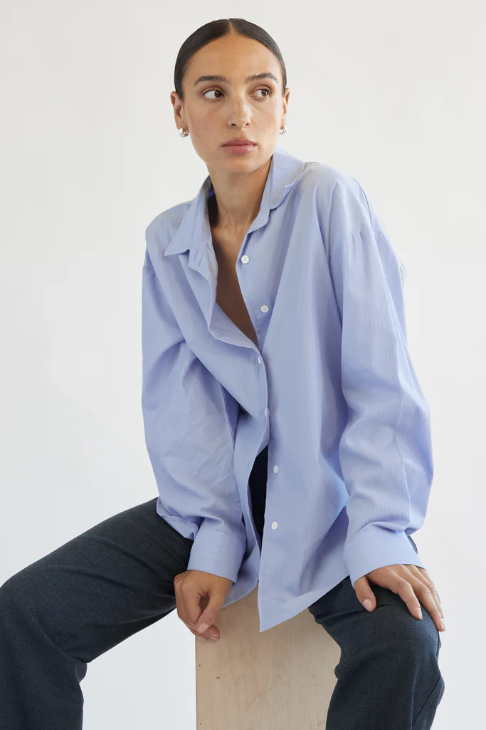 Woman wearing a light blue oversized shirt with a plain background