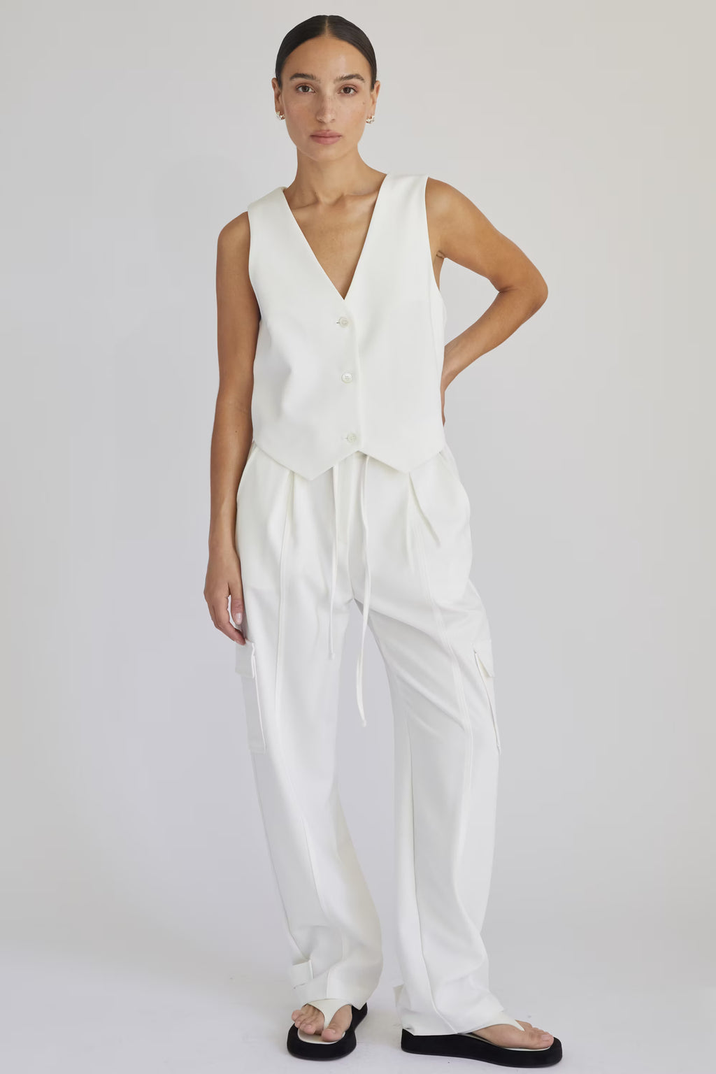 Woman wearing a white sleeveless top and pants on a plain background