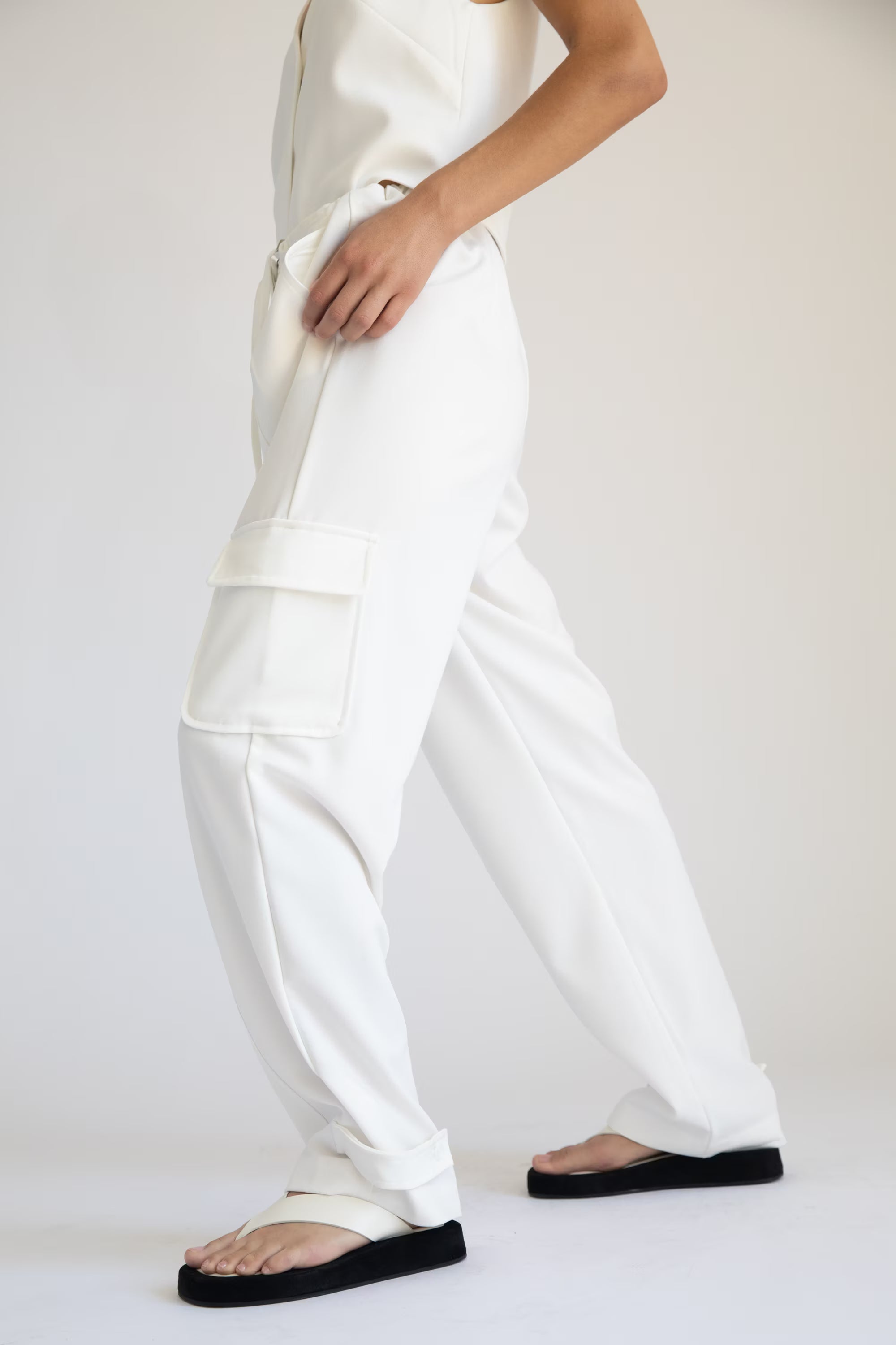 Person wearing white pants and black sandals on a plain background