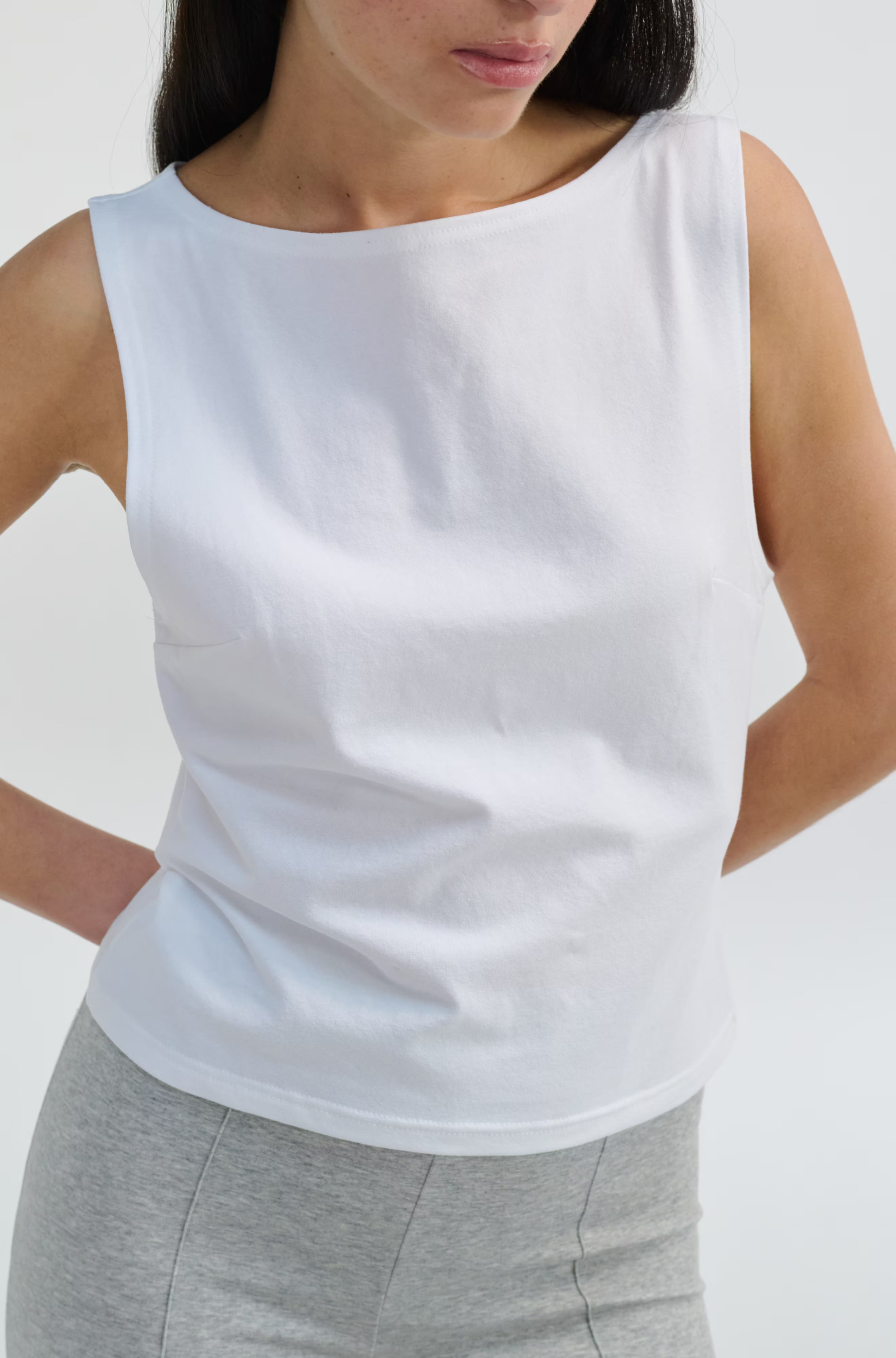 Person wearing a white sleeveless top and gray pants on a light gray background