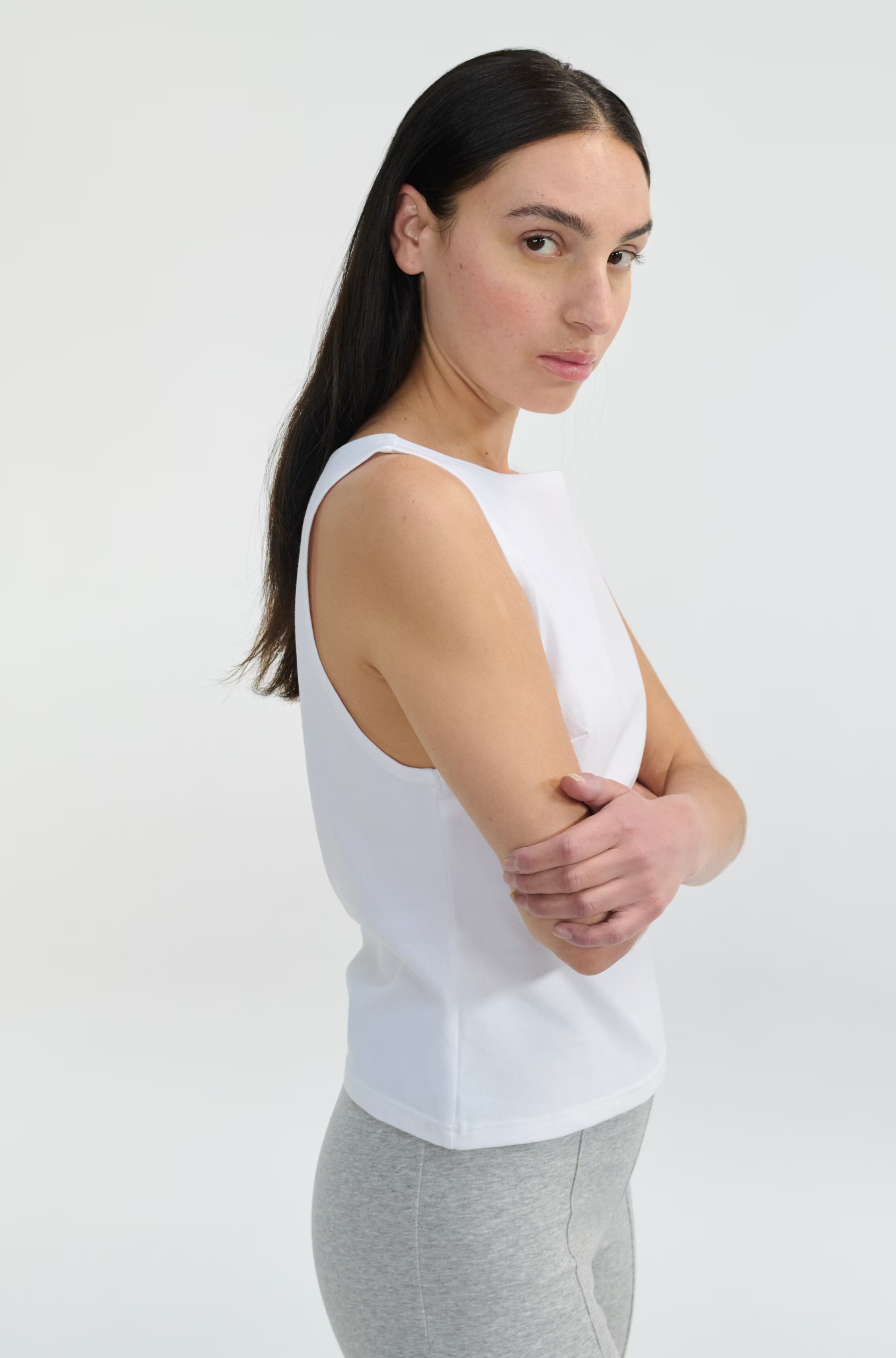 Woman wearing a white sleeveless top and gray pants on a white background