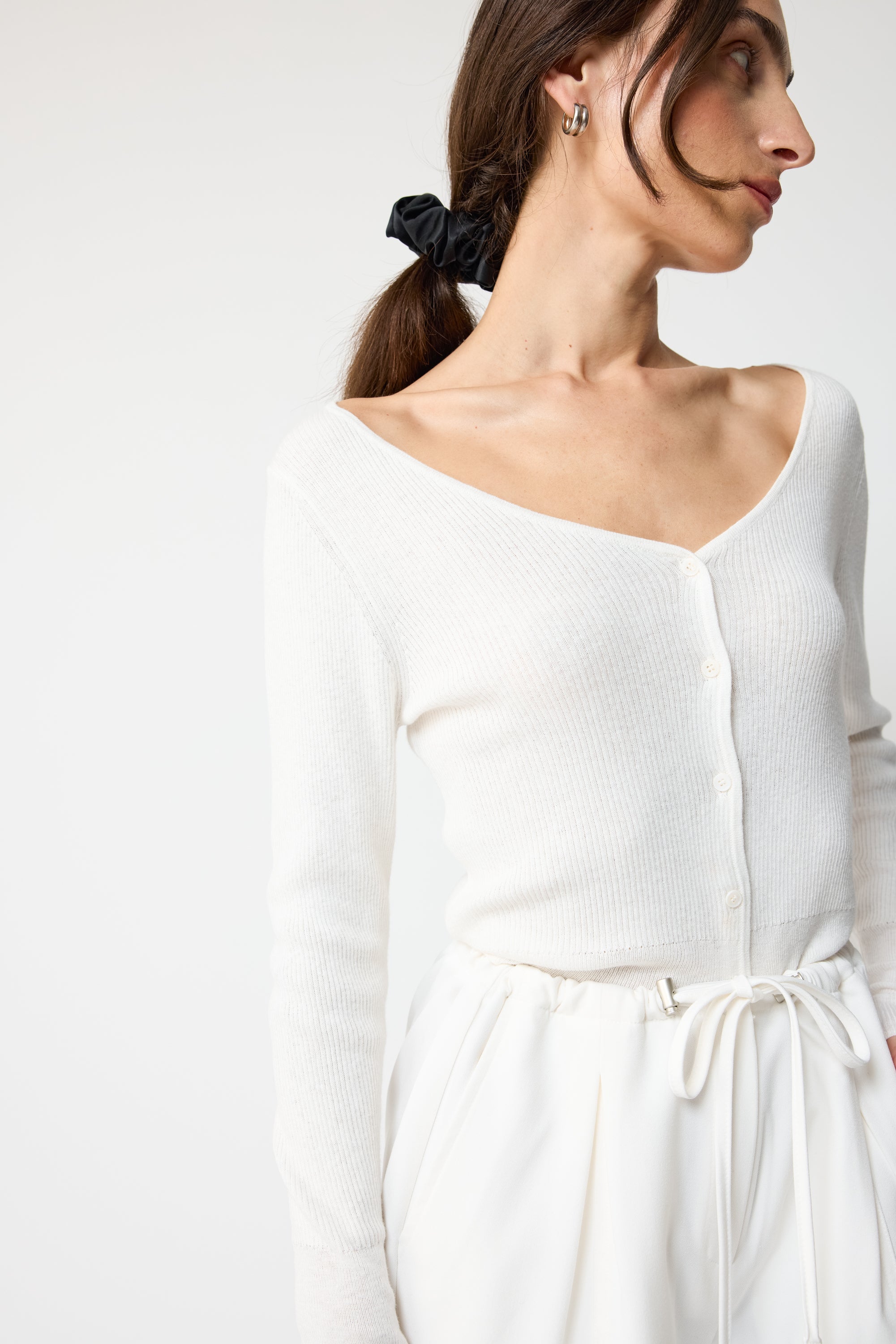 Woman wearing a white long-sleeve top with a V-neckline on a plain background