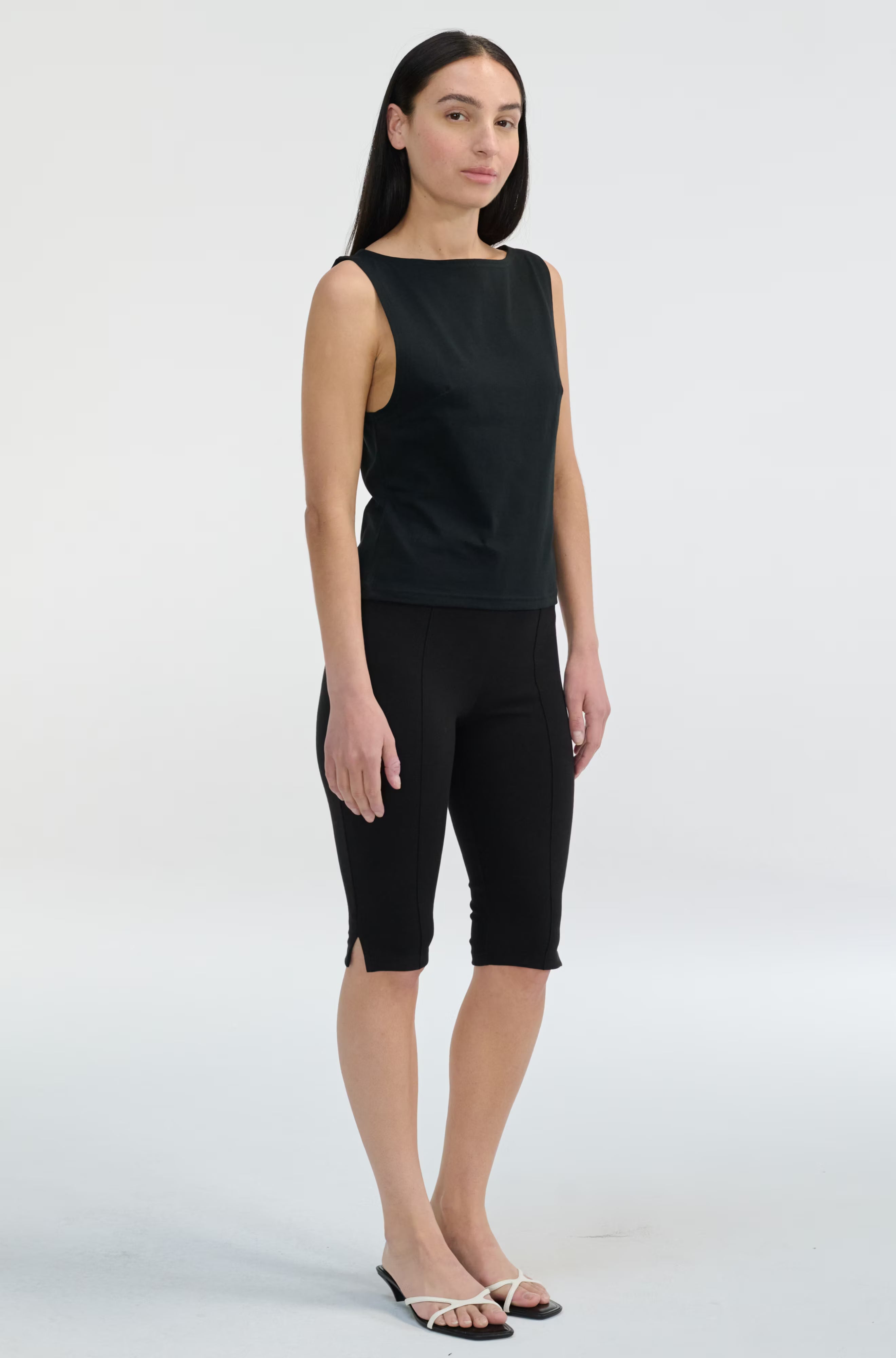 Woman wearing a black sleeveless top and black capri pants on a white background