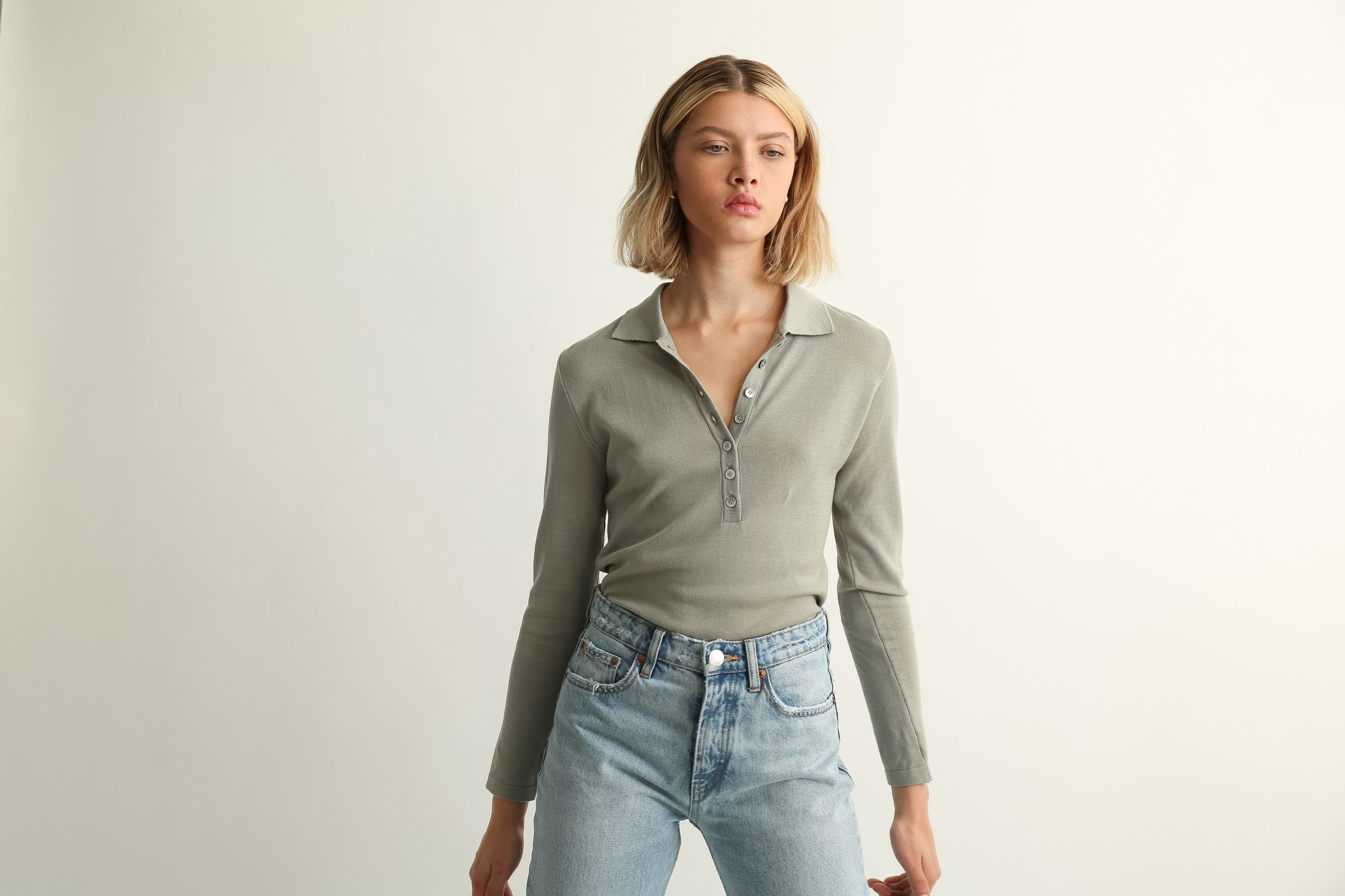 Woman wearing a green long-sleeve shirt and light blue jeans against a plain background