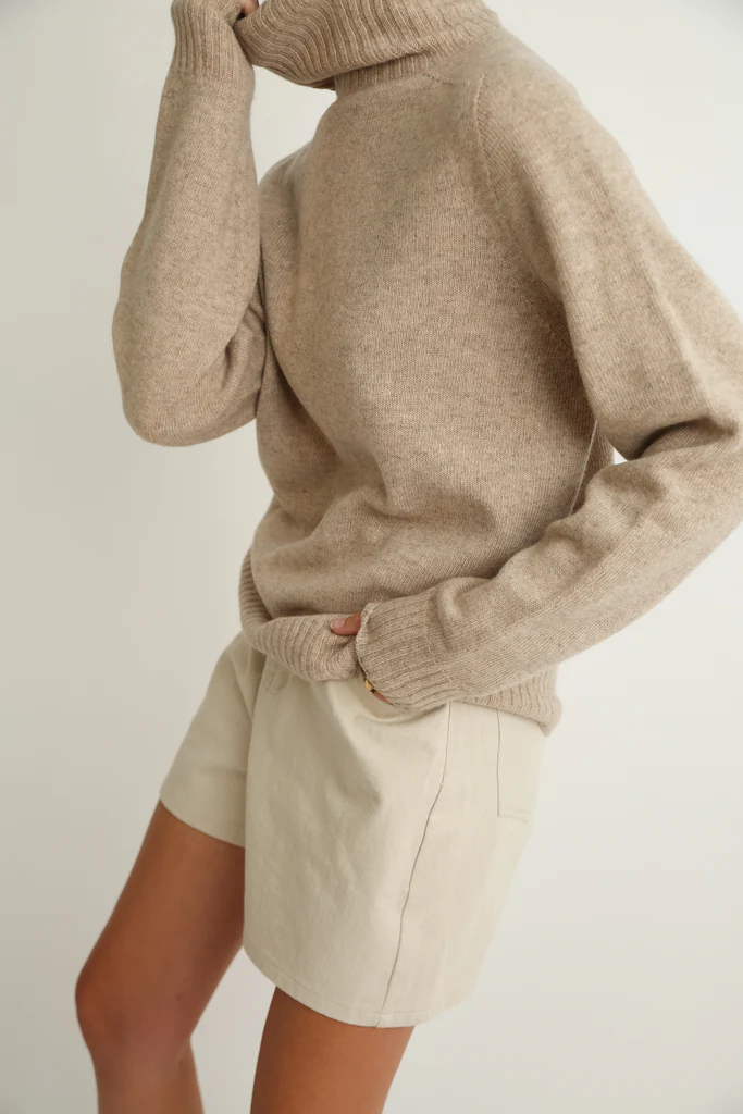 Person wearing a beige sweater and shorts on a plain background