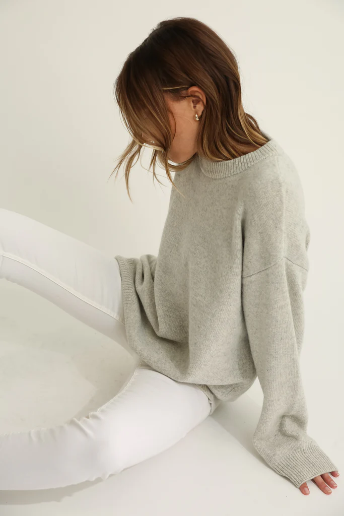 Person wearing a gray sweater and white pants on a light background