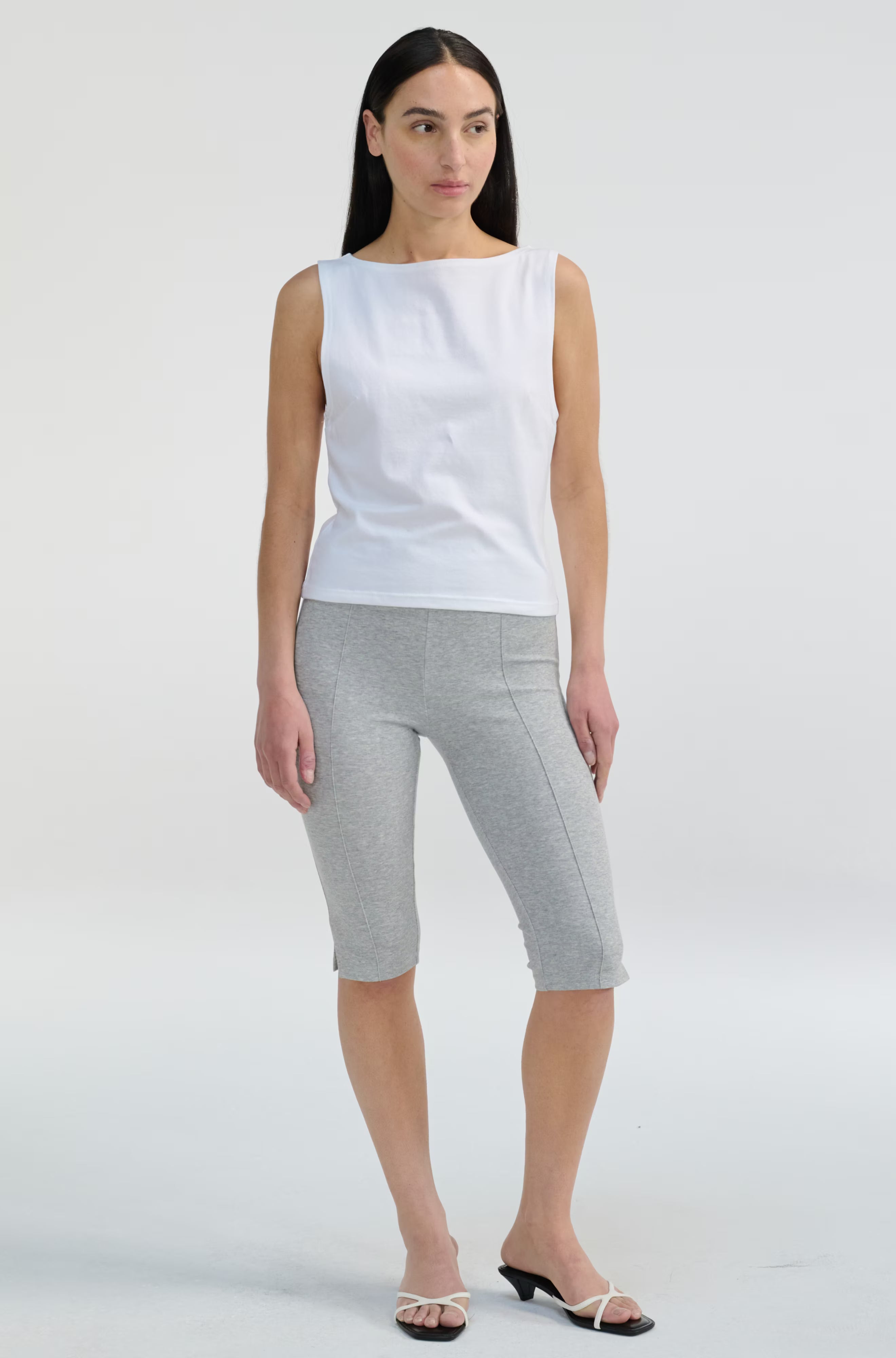 Woman wearing a white sleeveless top and gray shorts on a white background