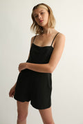 Woman wearing a black romper against a plain background