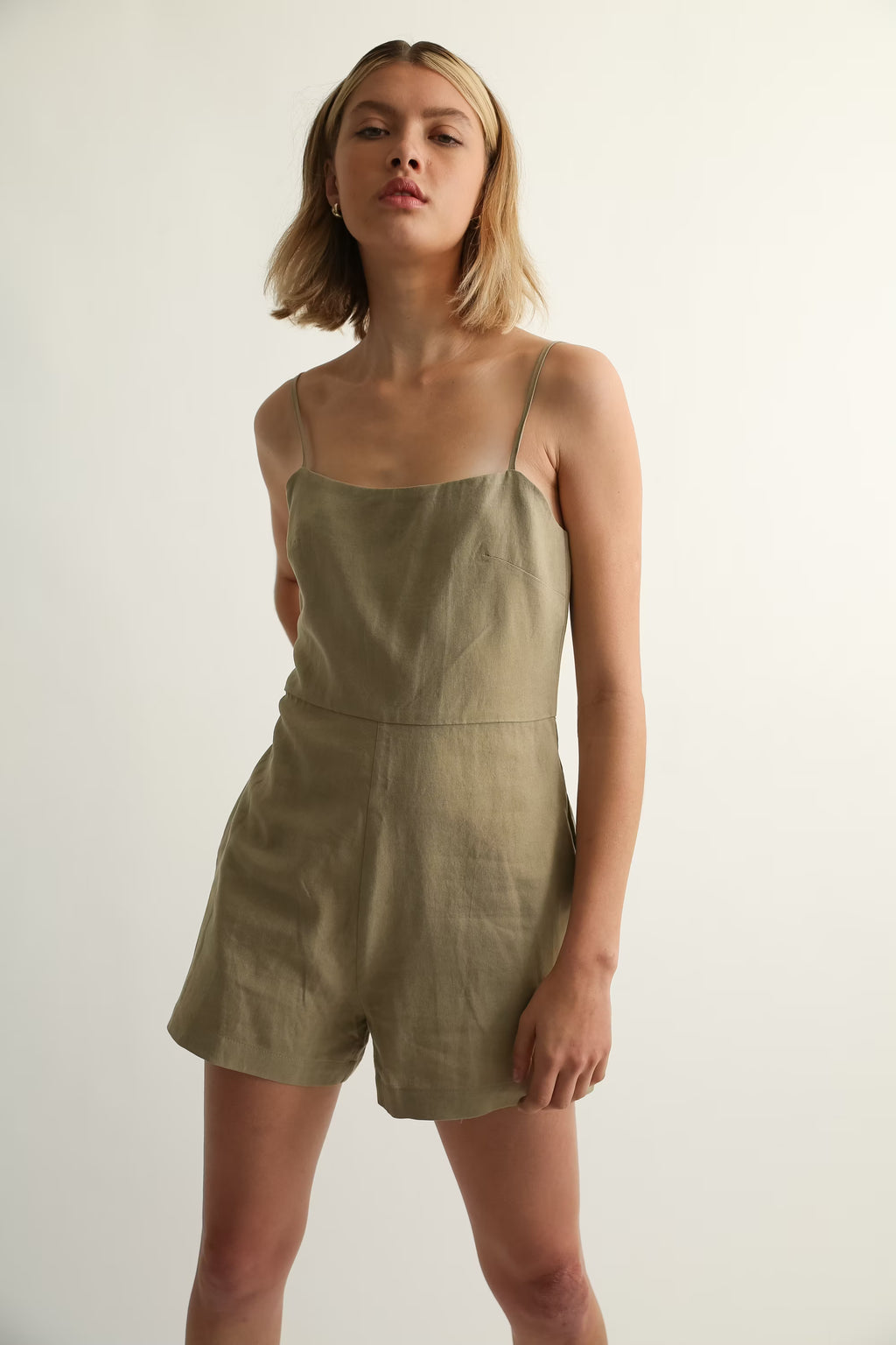 Woman wearing a green linen romper against a plain background