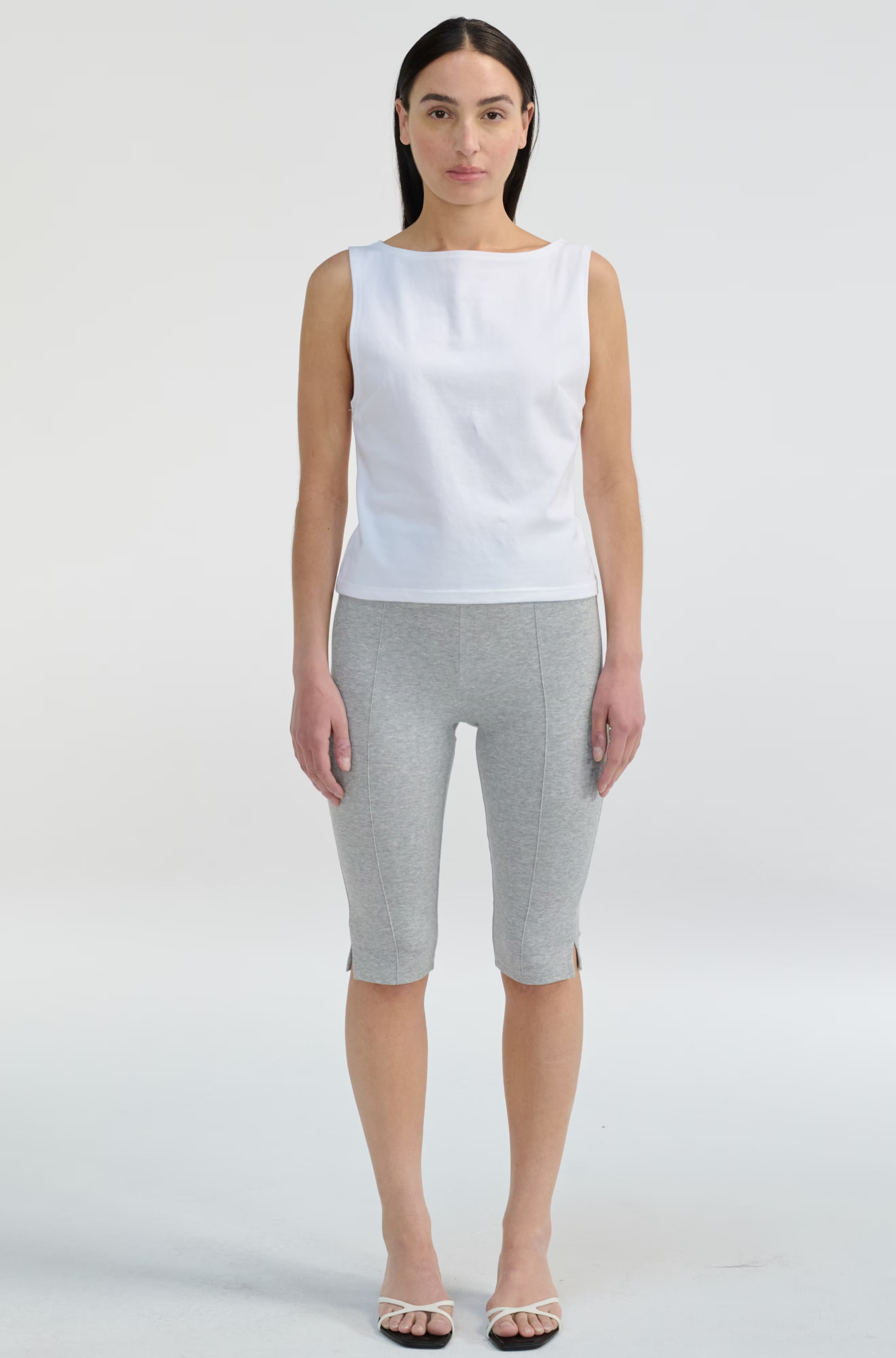 Woman wearing a white sleeveless top and gray shorts on a white background