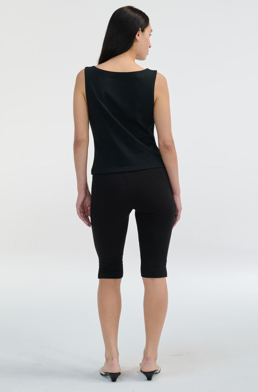 Woman wearing a black sleeveless top and black capri pants on a white background