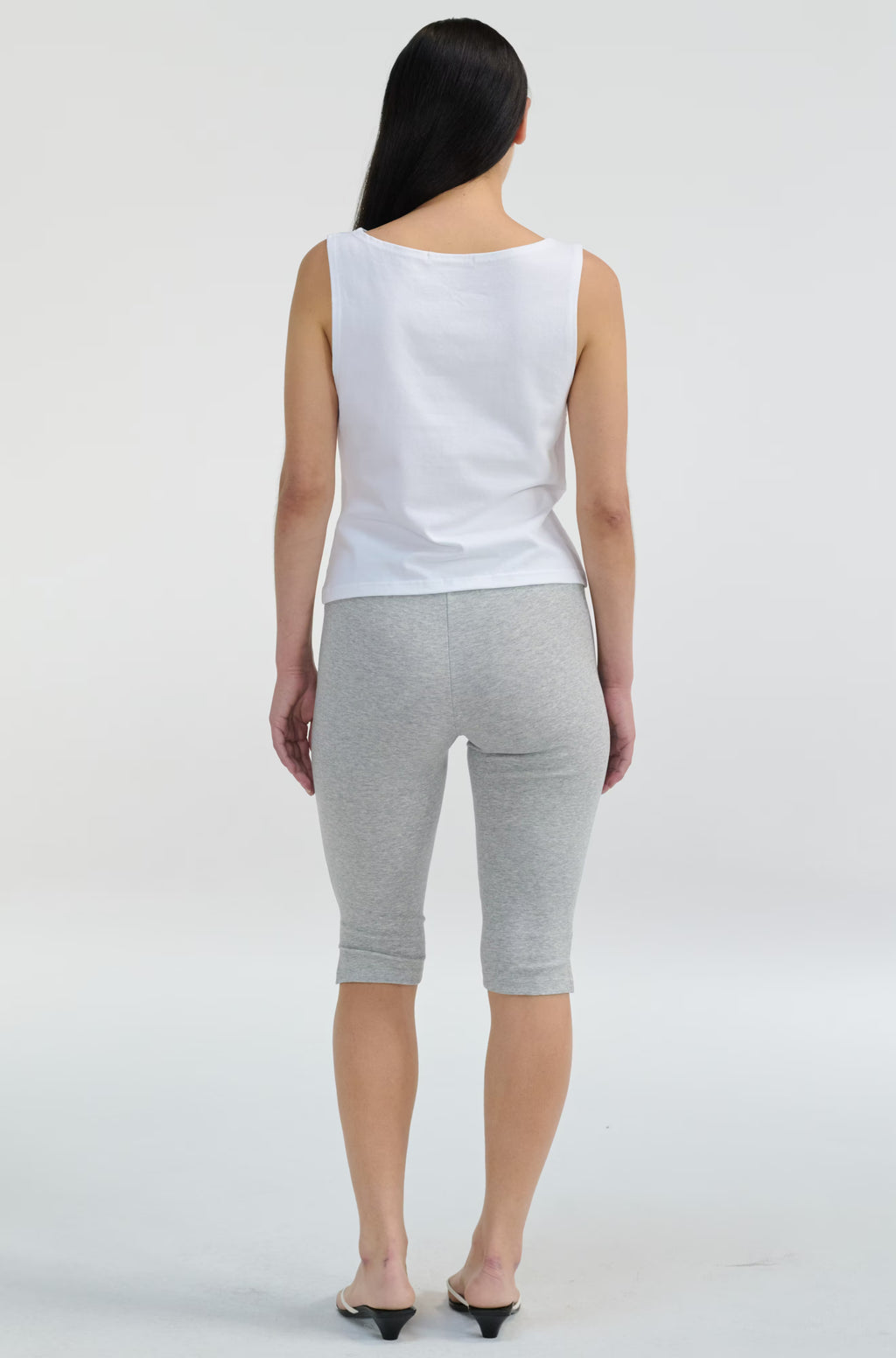 Woman wearing a white sleeveless top and gray shorts on a white background