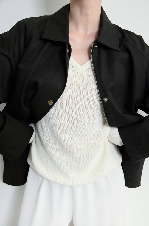 Person wearing a black jacket over a white sweater and pants on a plain background