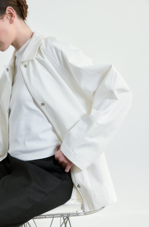 Person wearing a white jacket sitting on a chair against a white background
