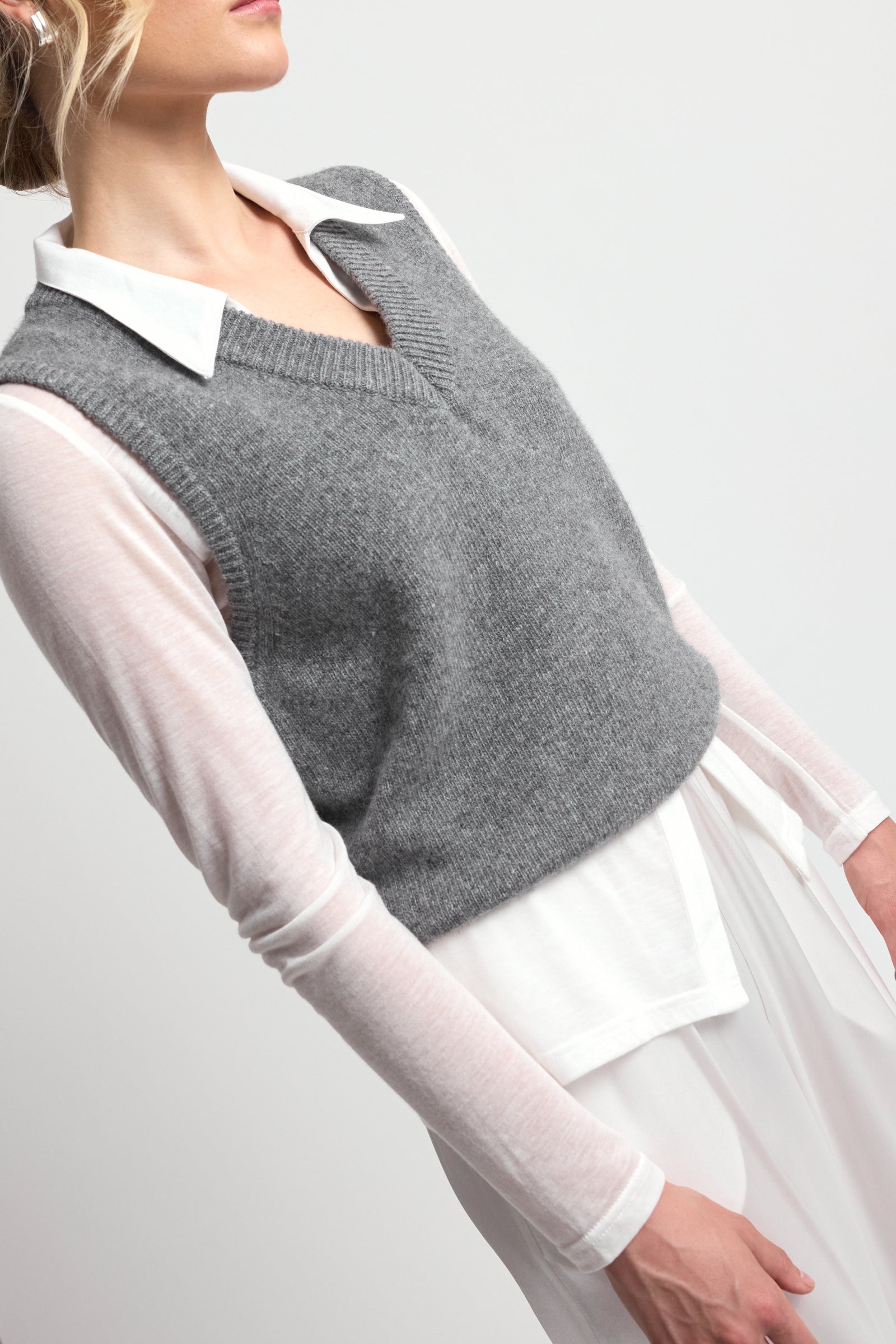 Gray knitted vest over a white shirt and sheer white sleeves on a plain background