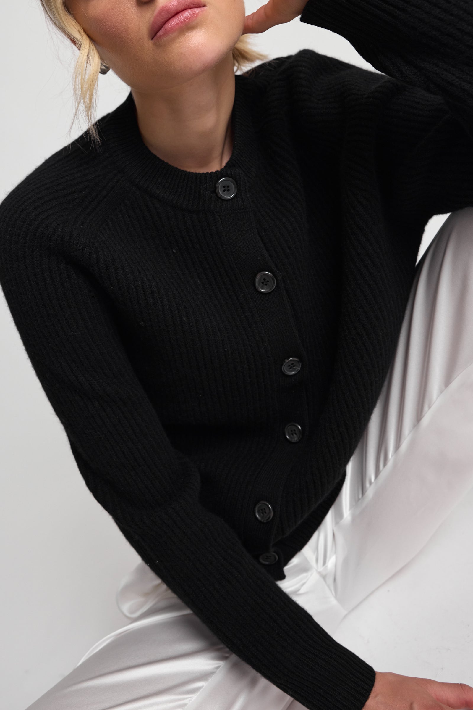 Woman wearing a black ribbed cardigan over a white outfit on a light background