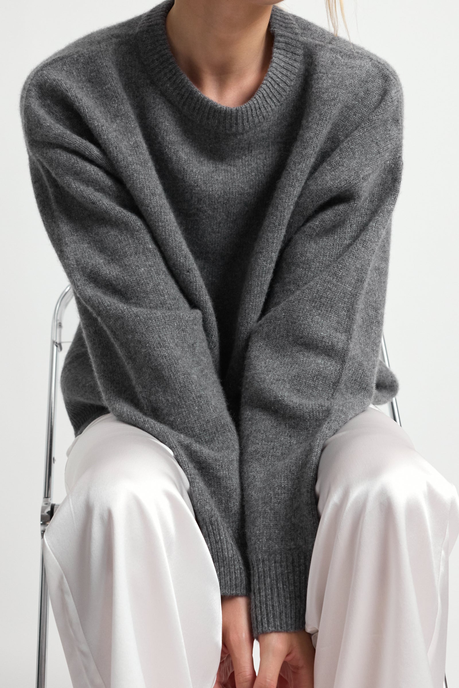 Woman wearing a gray wool sweater and white pants sitting on a chair.