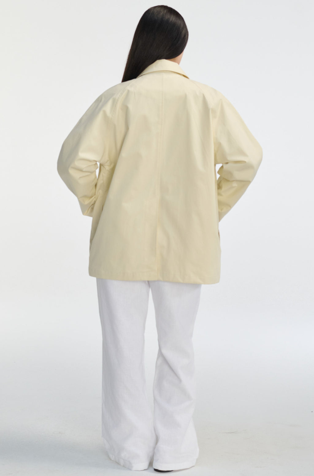 Person wearing a light-colored coat and white pants on a white background