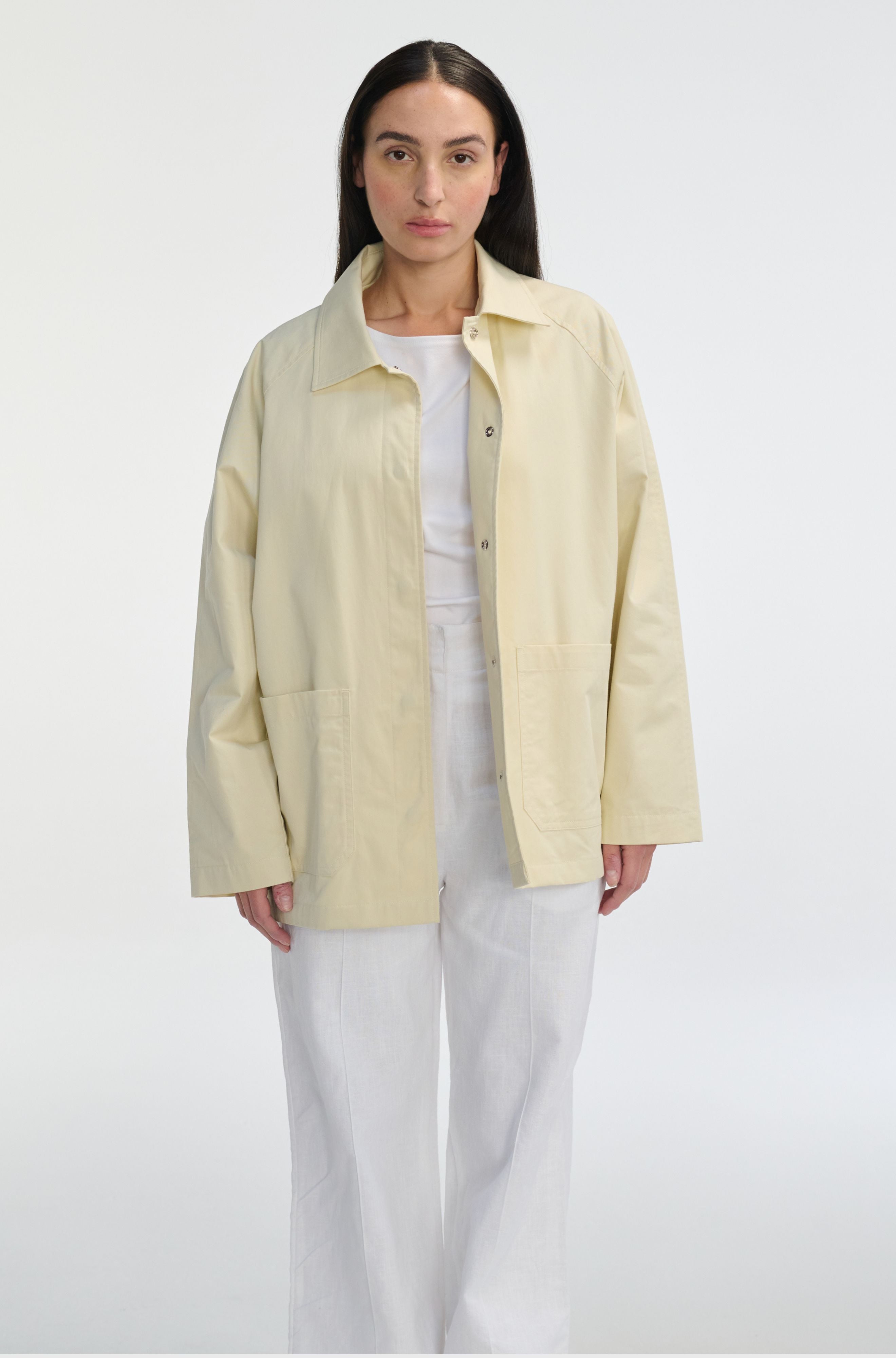 Woman wearing a light yellow jacket over a white shirt and pants on a white background