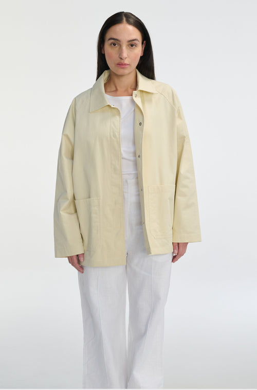 Woman wearing a light yellow jacket over a white shirt and pants on a white background