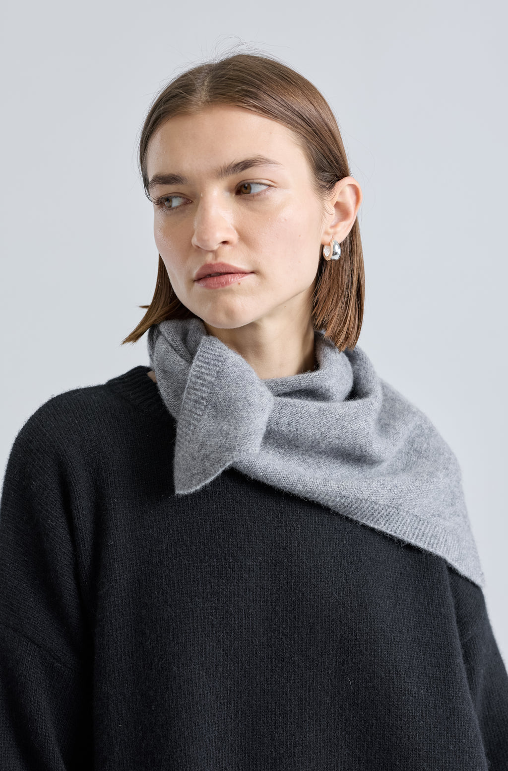 Woman wearing a grey scarf over a black outfit on a light grey background