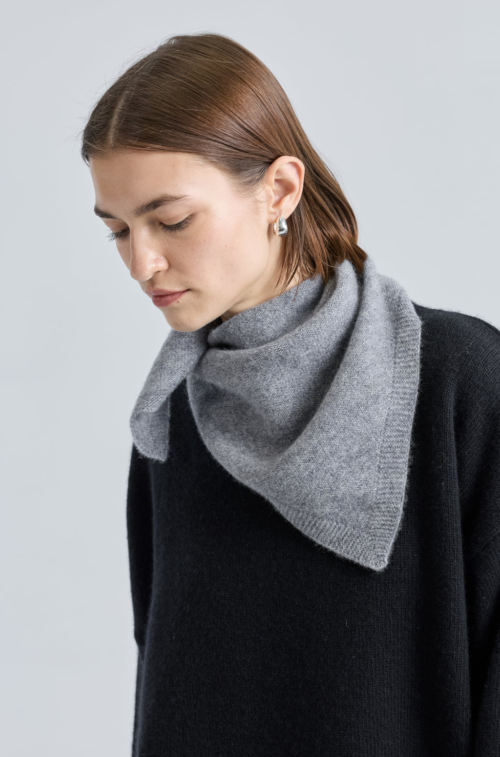 Woman wearing a grey scarf over a black outfit on a light grey background
