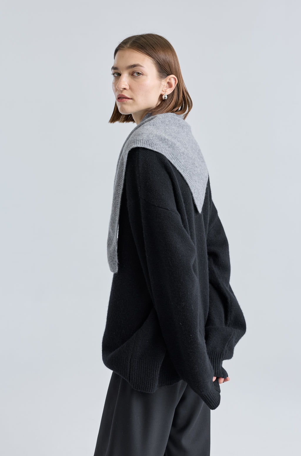 Woman wearing a grey scarf over a black outfit on a light grey background