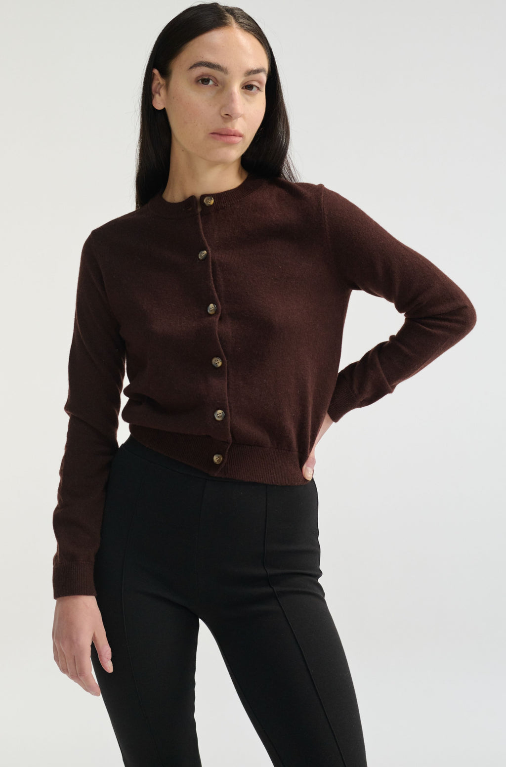 Woman wearing a brown button-up cardigan and black pants on a white background