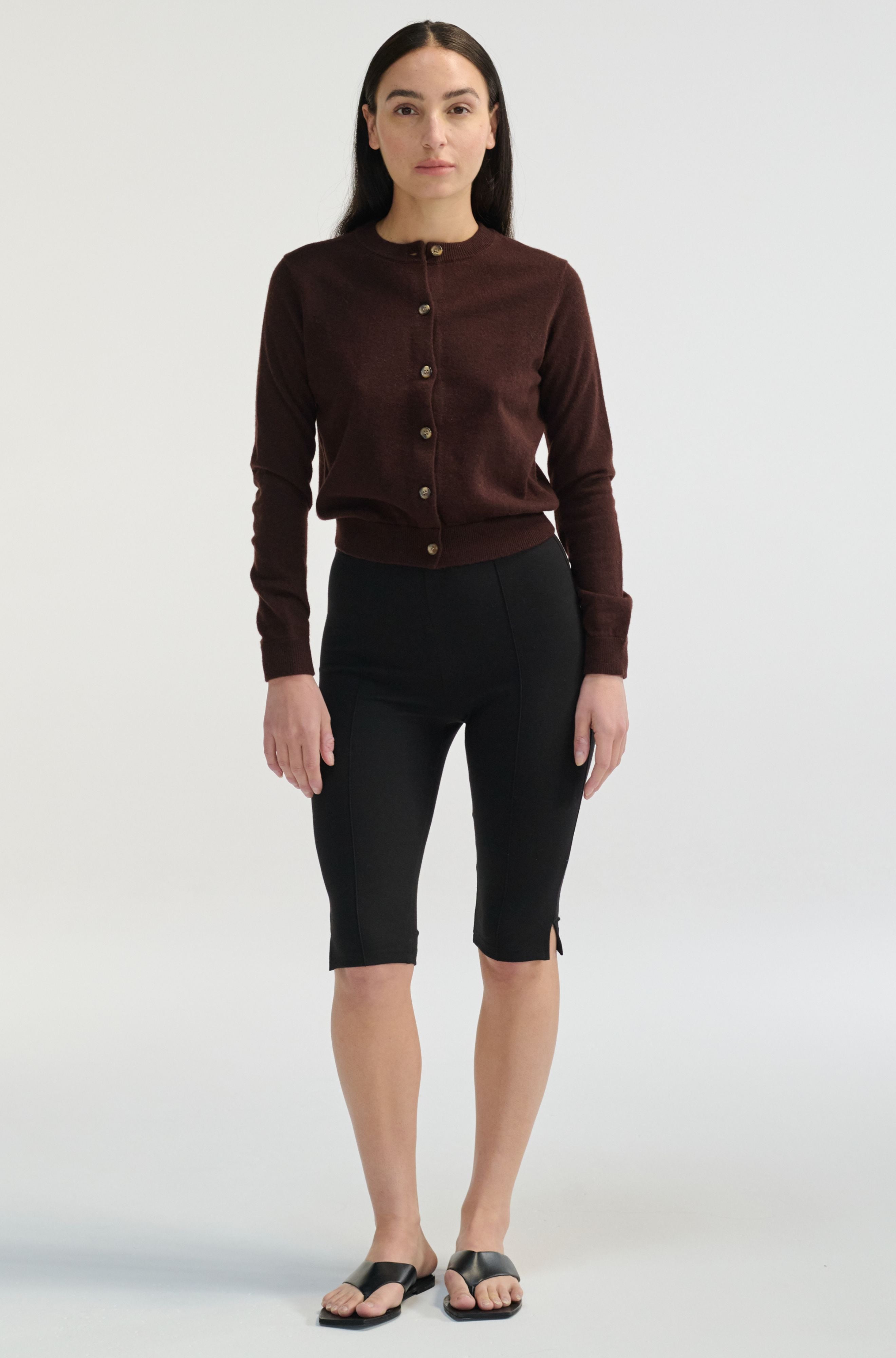 Woman wearing a brown cardigan and black pants on a white background