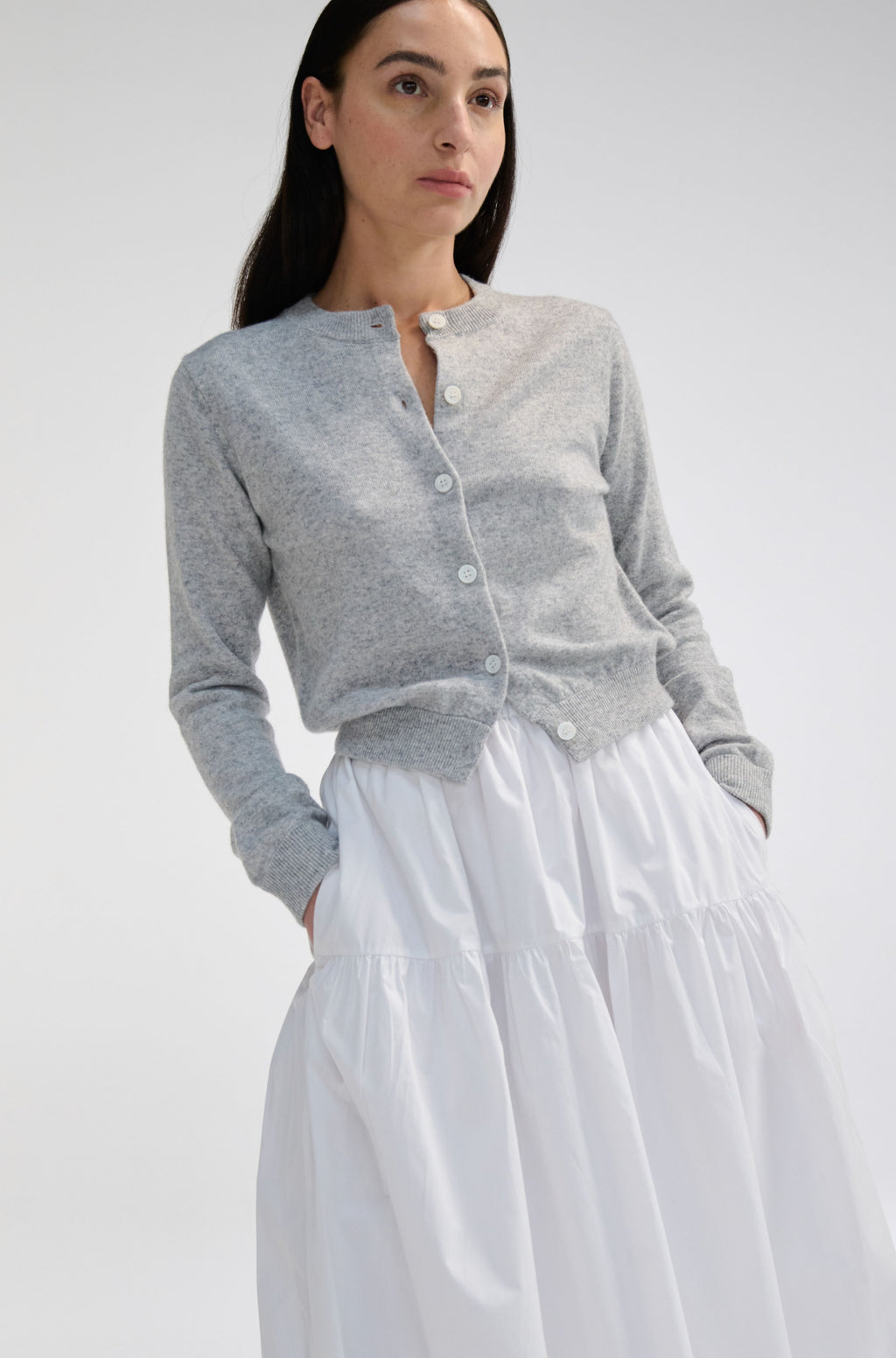 Woman wearing a gray cardigan over a white skirt on a plain background