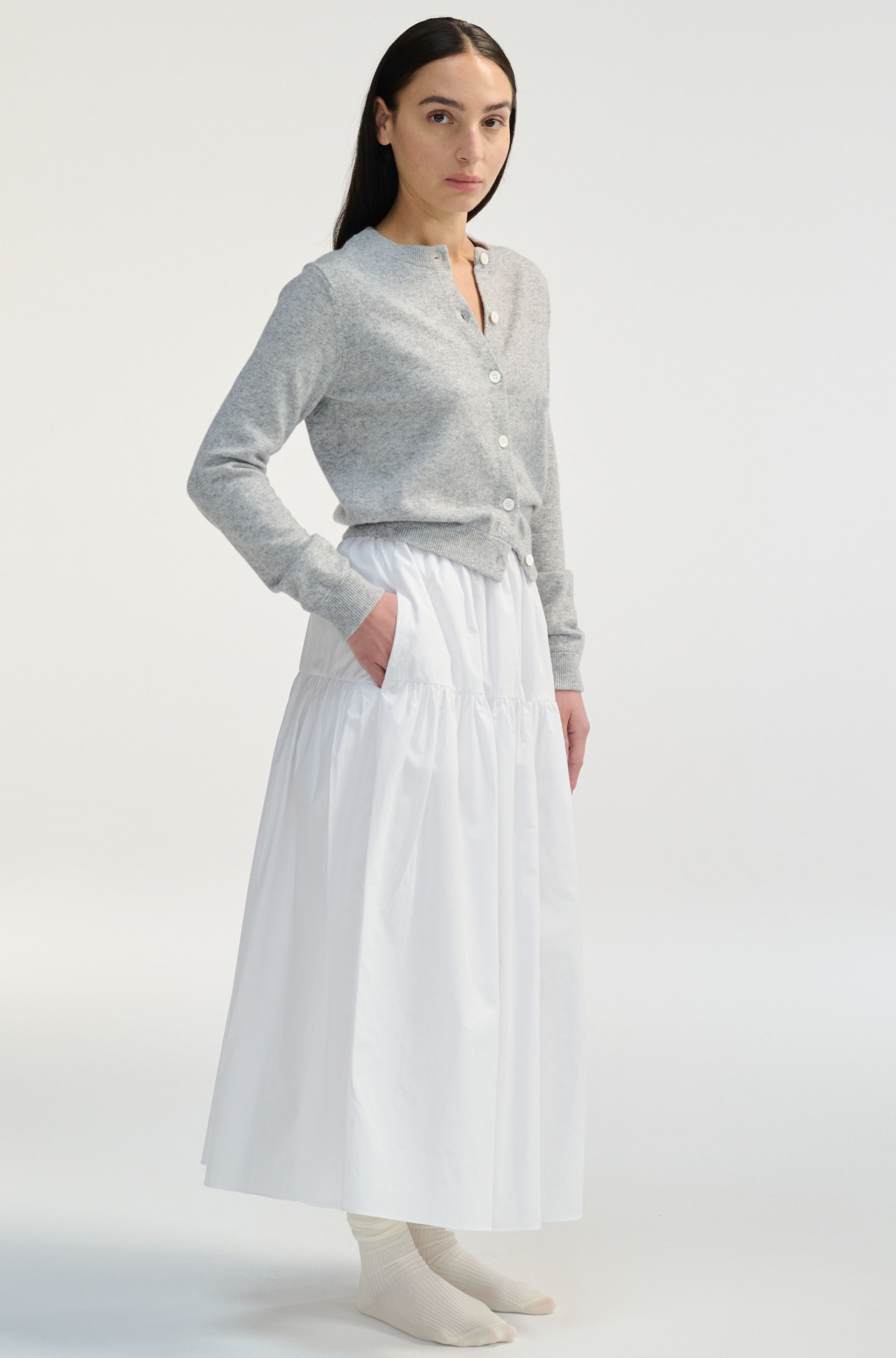Woman wearing a gray cardigan and white skirt on a white background
