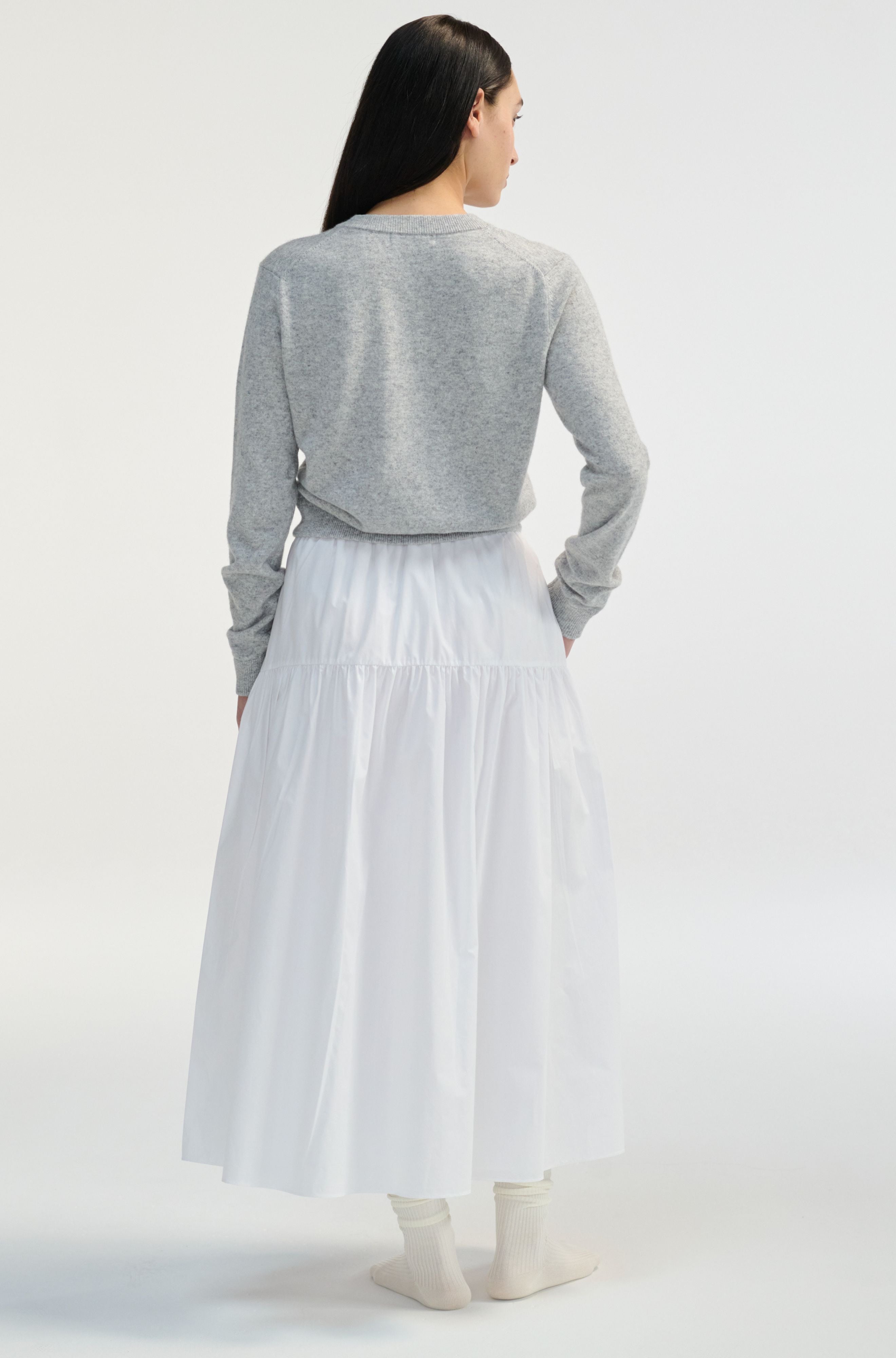 Woman wearing a gray sweater and white skirt on a white background