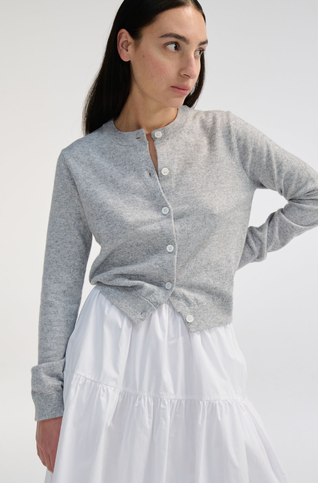 Woman wearing a gray cardigan over a white skirt on a plain background