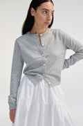 Woman wearing a gray cardigan over a white skirt on a plain background
