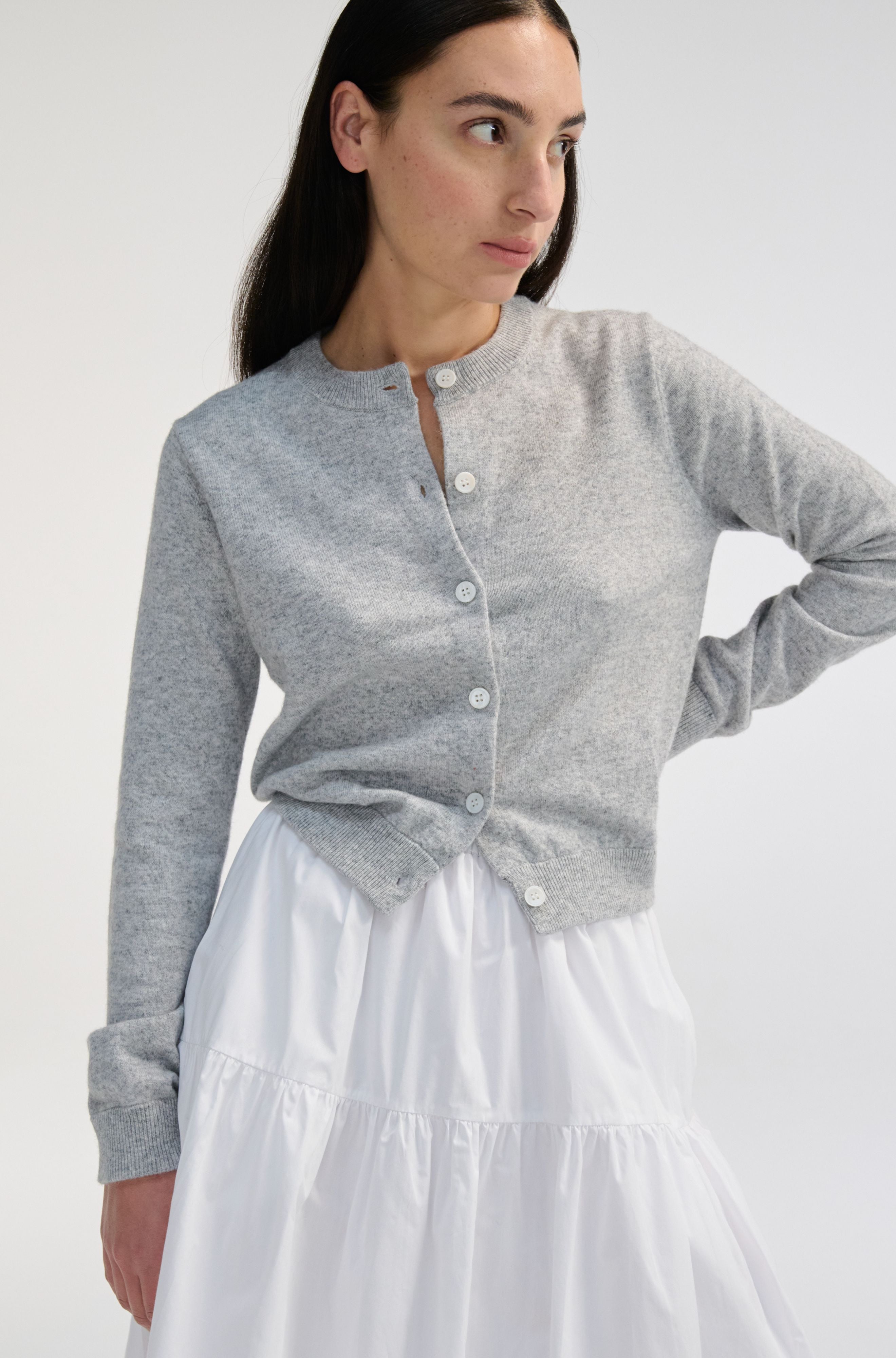 Woman wearing a gray cardigan over a white skirt on a plain background