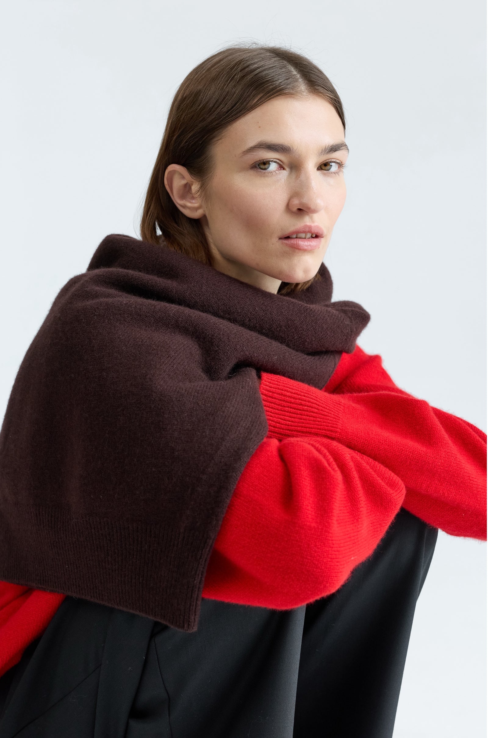 Woman wearing a brown sweater over a red sweater with a white background