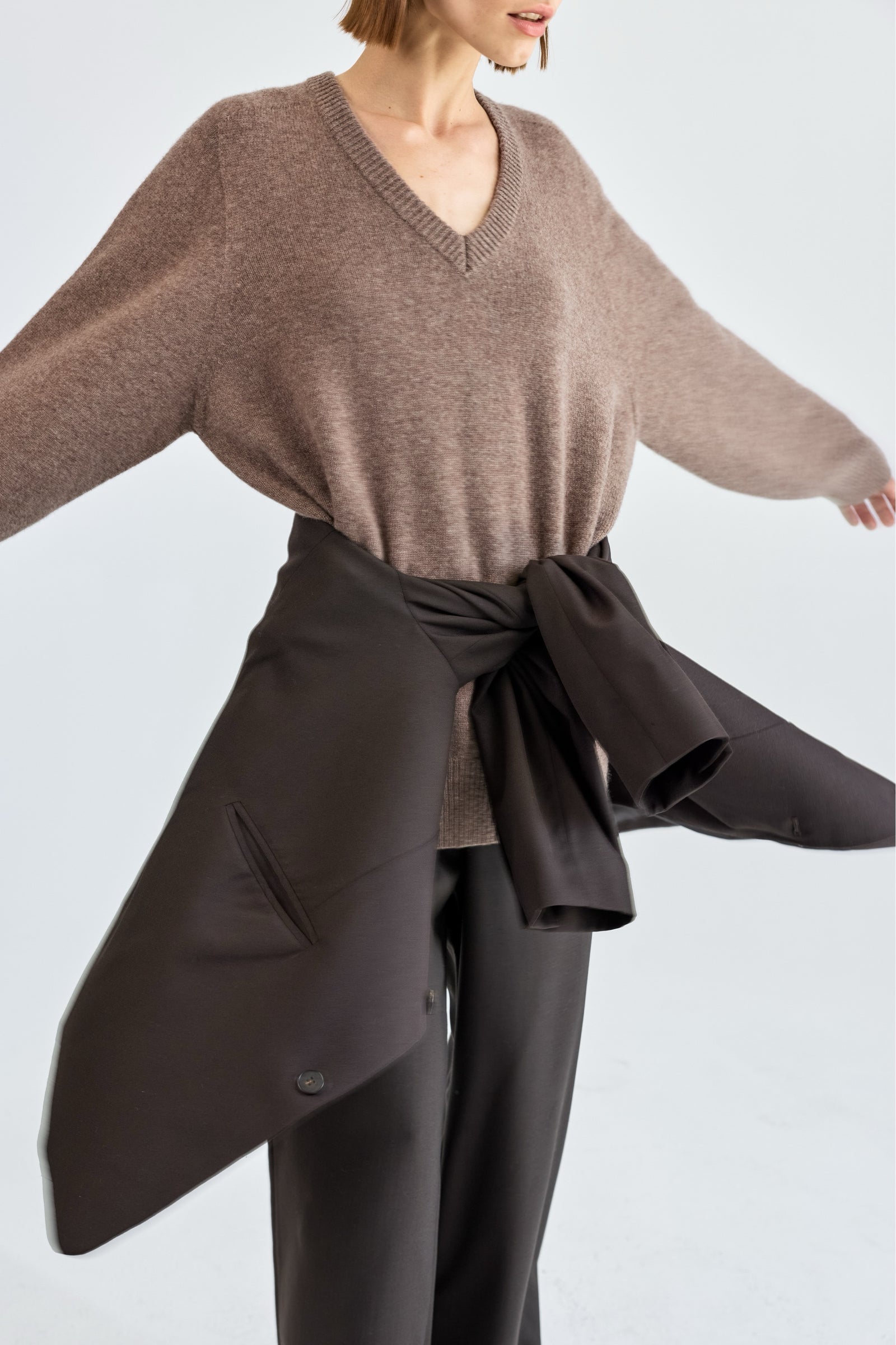 Woman wearing a brown sweater and dark brown blazer over pants on a light gray background