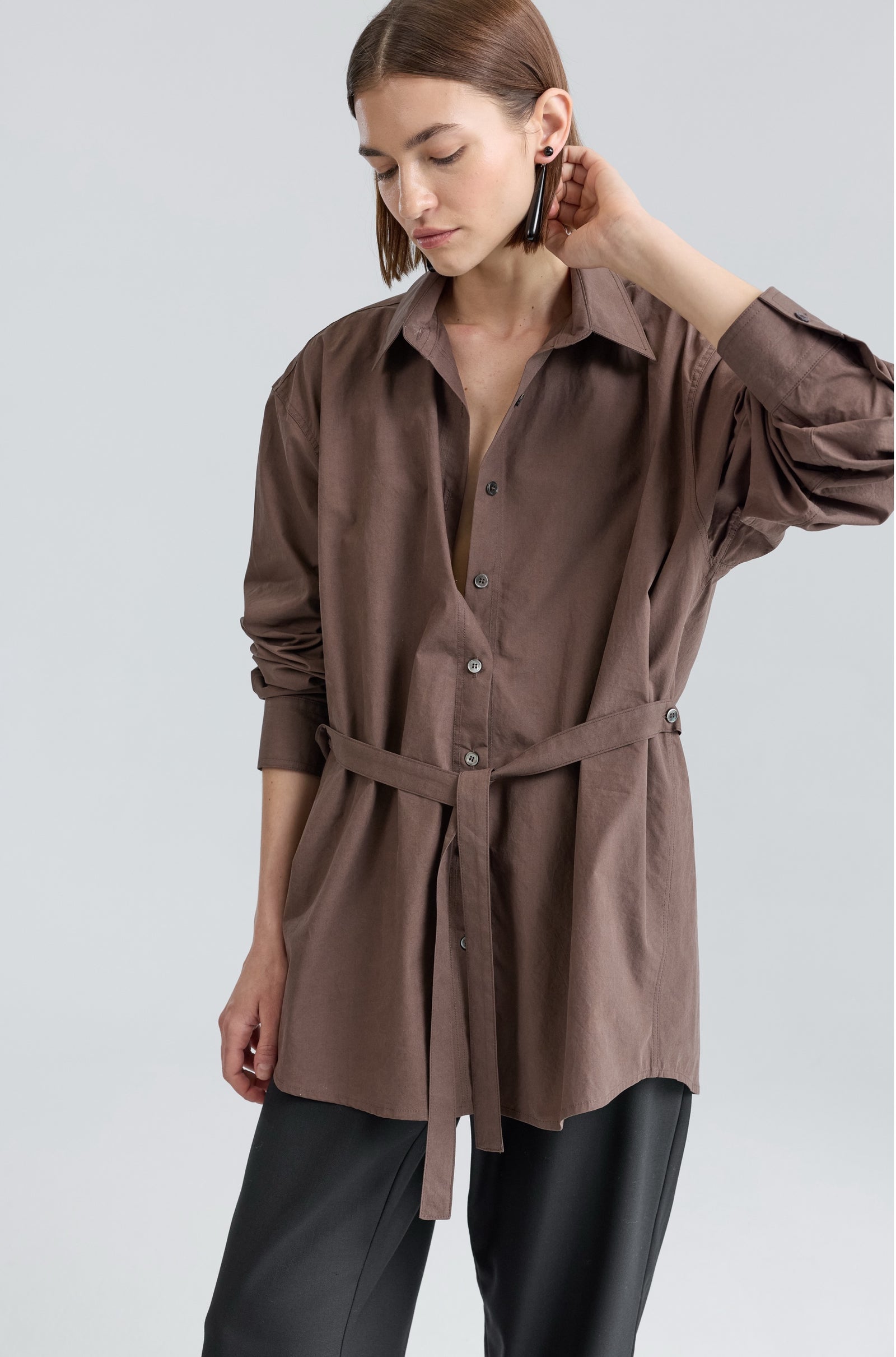 Woman wearing a brown button-up shirt with a belt on a light gray background