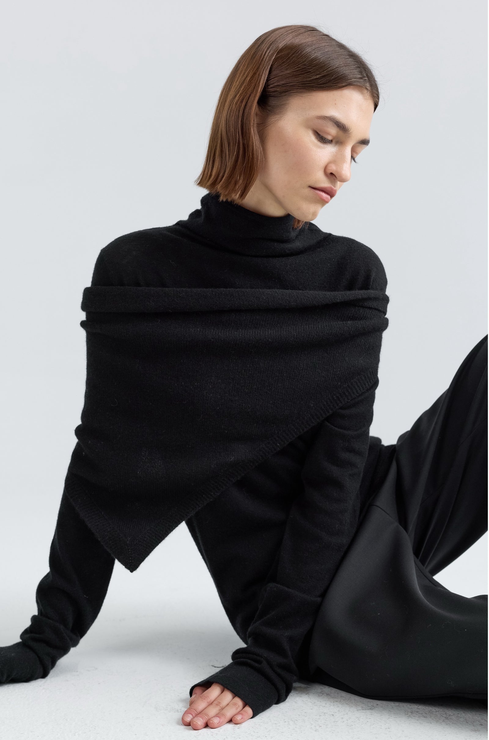 Woman wearing a black turtleneck top with a large scarf on a light gray background