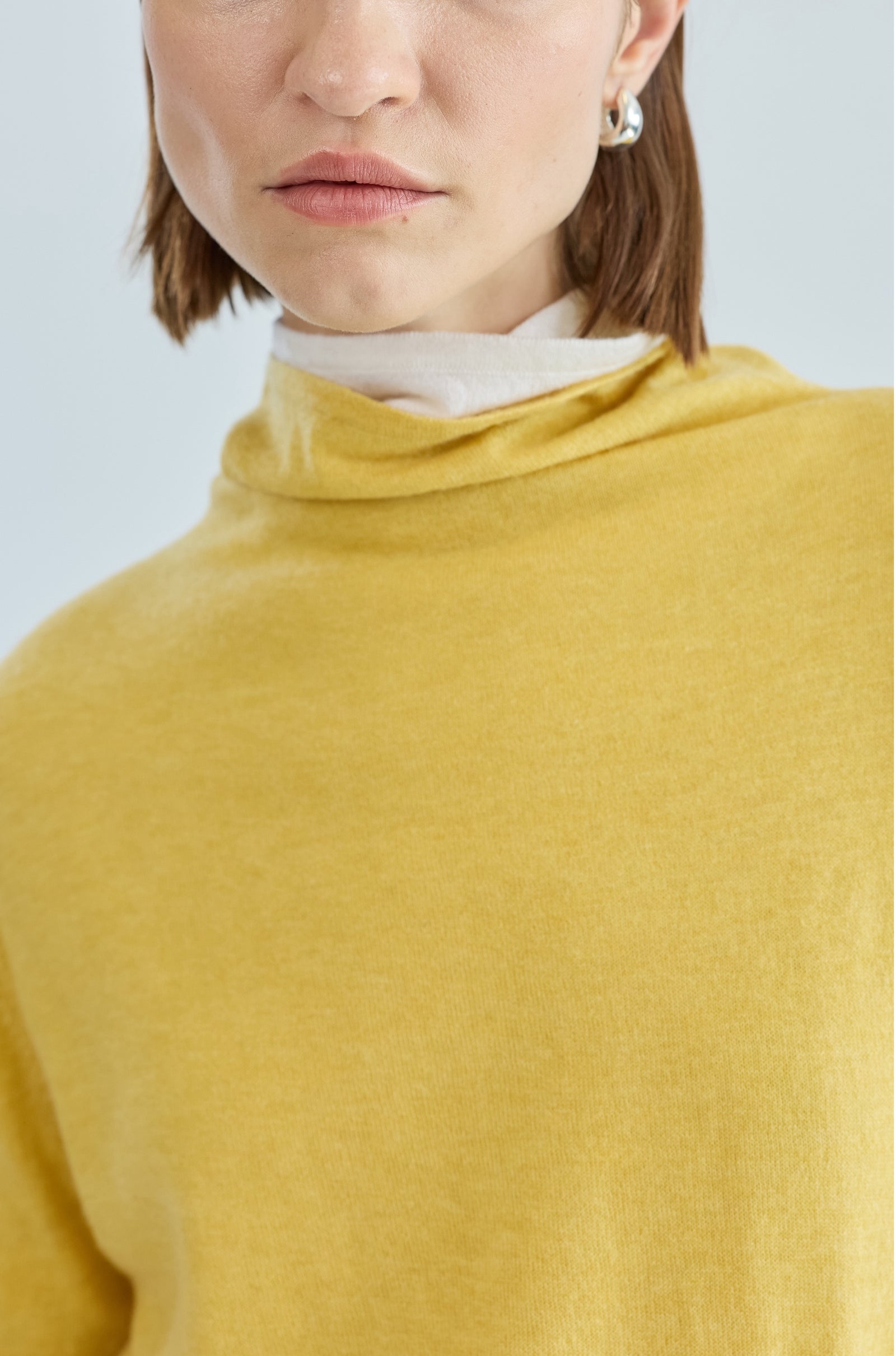 Person wearing a mustard yellow sweater with a plain background