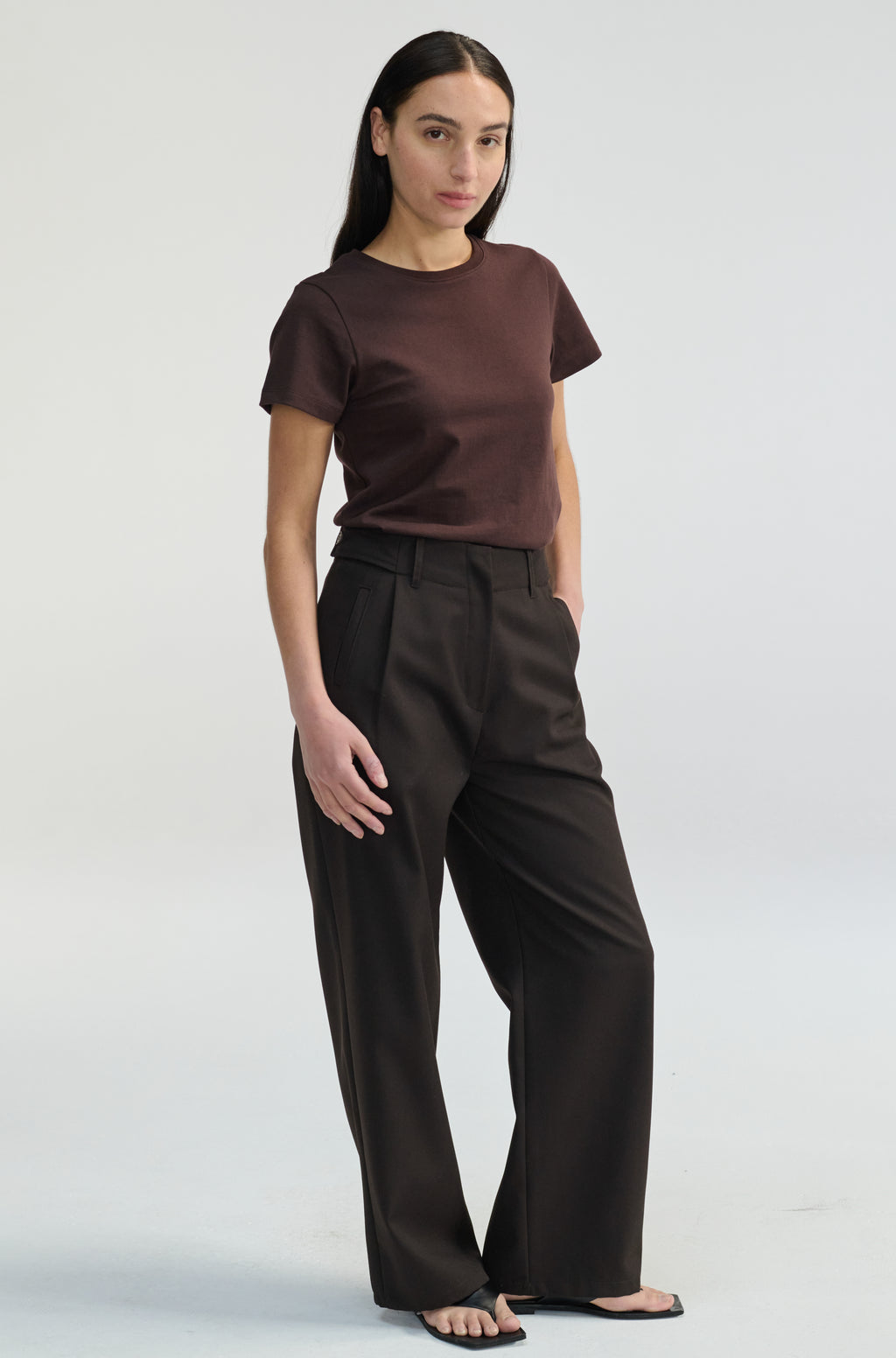 Woman wearing a brown t-shirt with dark brown trousers on a plain background
